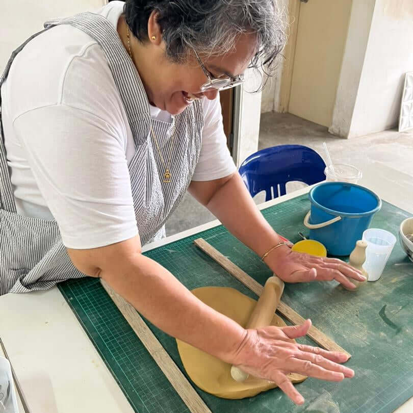 Independent pottery studio access with a smiling woman shaping clay using a rolling pin and tools.