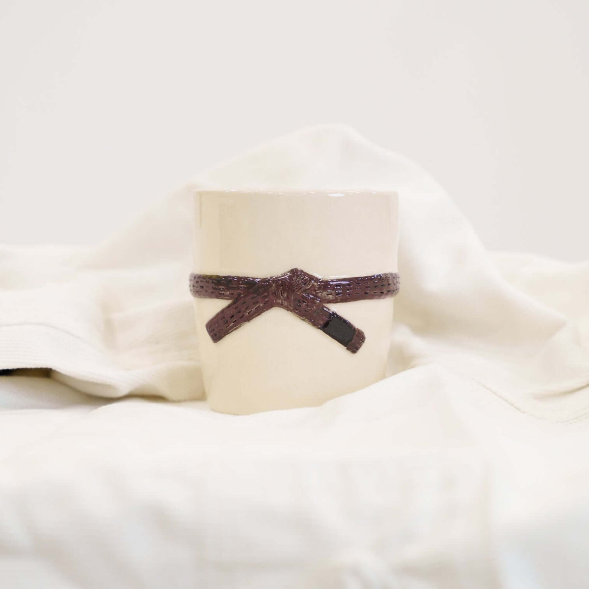 A cream colored mug with a brown brazilian jiu jitsu belt design