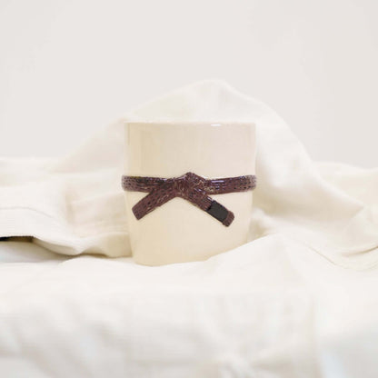 A cream colored mug with a brown brazilian jiu jitsu belt design